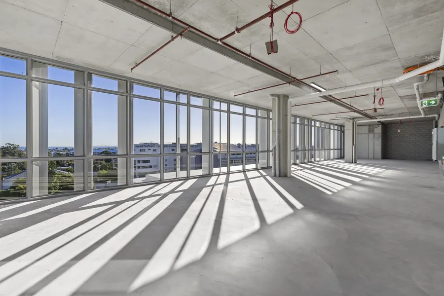 An empty cold-shell suite with full-height glazing and sunlight across a concrete floor